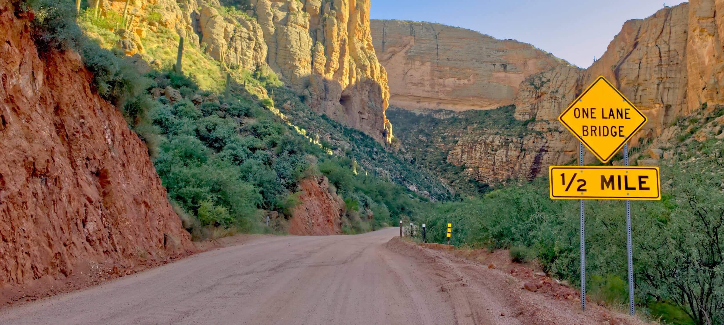 Dirt section of Arizona State Route 88 winding through rocky desert terrain, with a warning sign indicating a narrow road ahead.