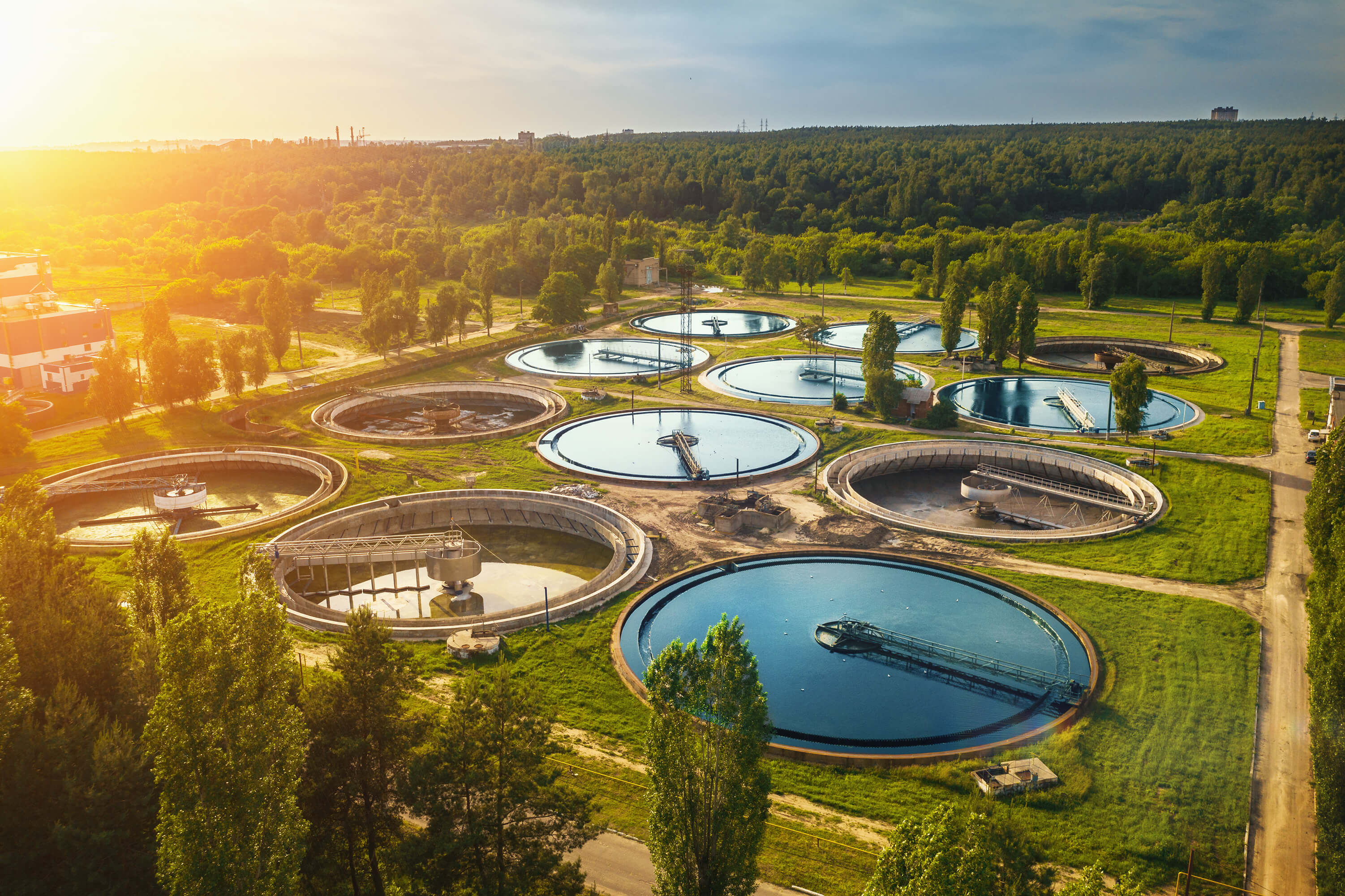 Aerial view of a wastewater treatment plant with multiple circular sedimentation tanks surrounded by greenery.