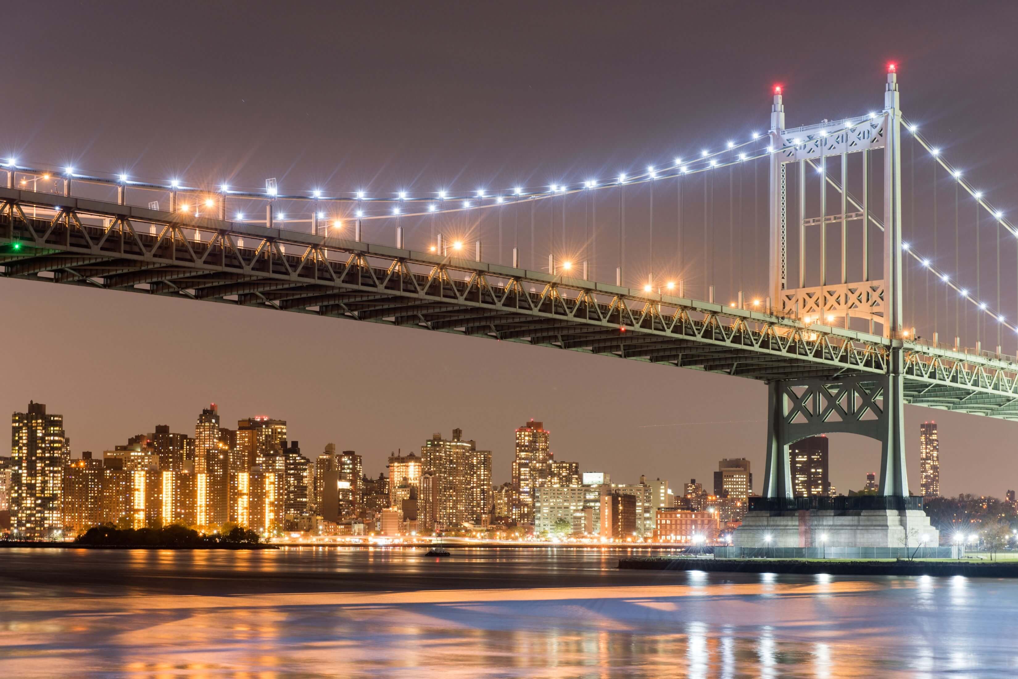 Illuminated RFK Bridge at night, spanning the East River with the New York City skyline in the background.